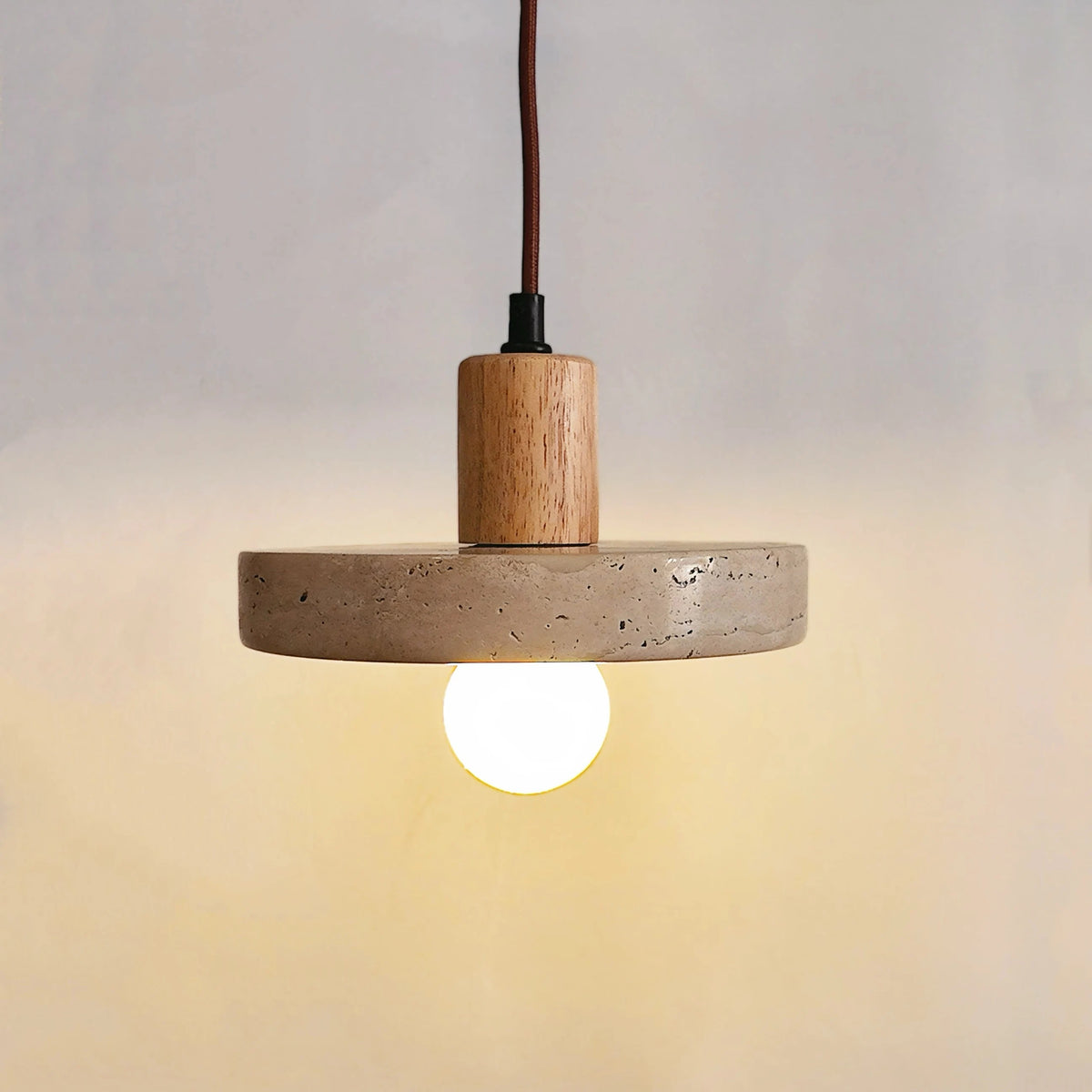 Natural stone disc pendant light with a light wood-tone top, switched on
