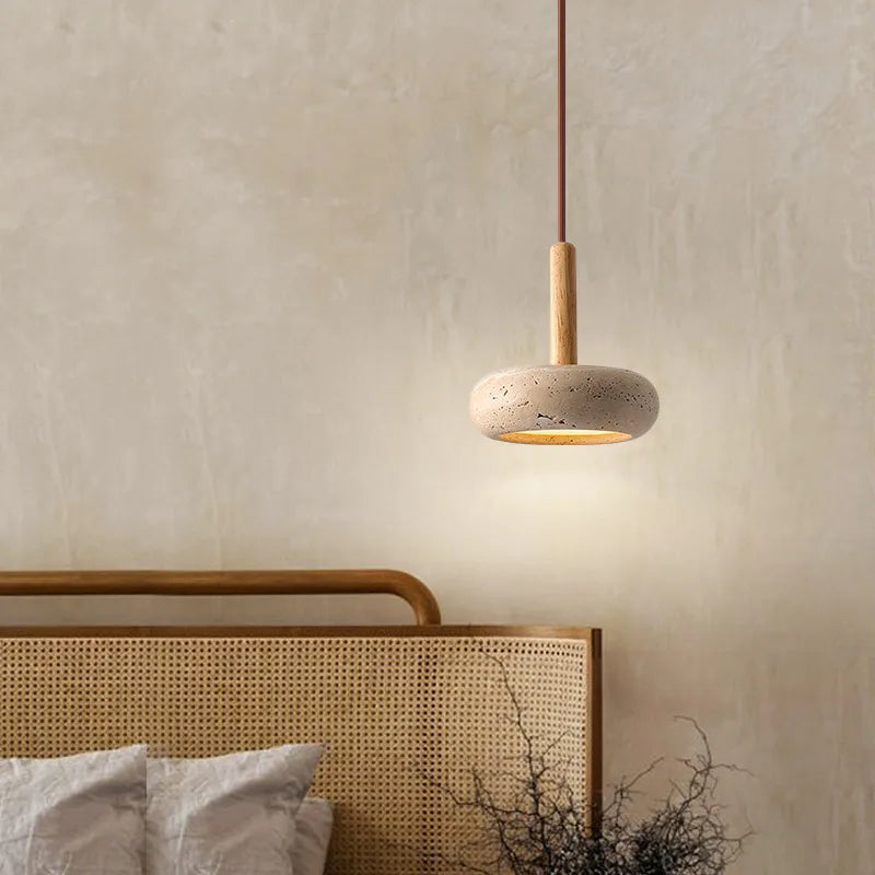 Travertine disc pendant light hanging beside a rattan headboard